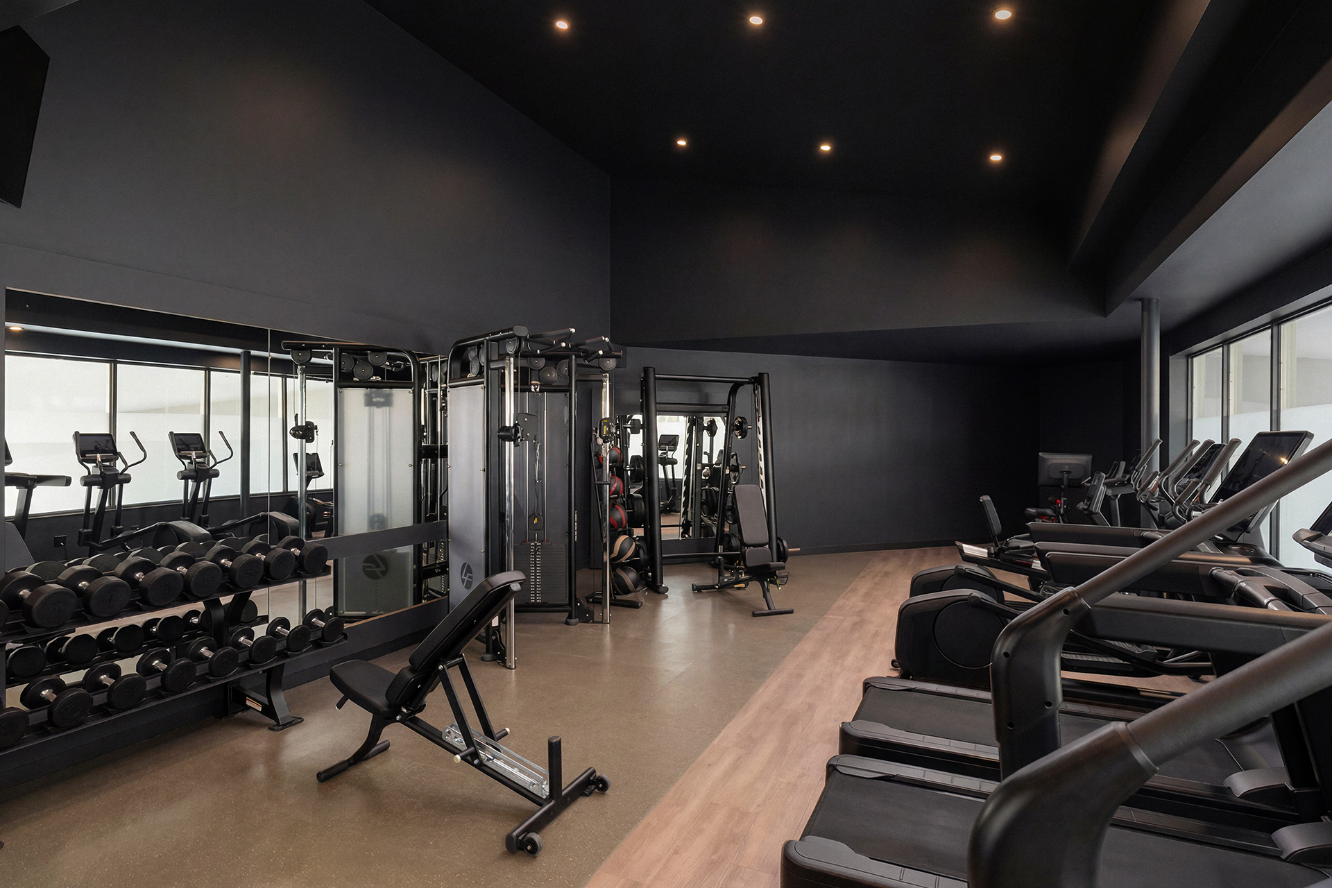 A large fitness center with light wood accents, a large mirror, cardio equipment, free weights and benches.